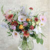 Loose garden-style bouquet of mixed pastel and bright flowers in a clear glass vase.