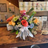 Mixed bouquet of roses, ranunculus, hydrangea, and daisies in a vase with a white ribbon