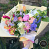 Hand-tied bouquet of mixed pastel roses, tulips, and other flowers wrapped in pale yellow paper