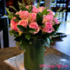 Pink roses arranged in a tall green vase with glossy foliage