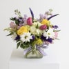 A spring mix of fresh flowers in a clear cube vase. A