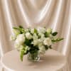 White floral arrangement in a clear glass vase on a draped table