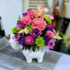 Pink and purple flowers arranged in a white unicorn planter