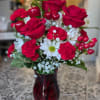 Tall red and white arrangement with red roses, red carnations, white daisies, and baby's breath in a red glass vase