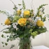 Tall arrangement of yellow roses, white snapdragons, and green accents in a clear glass vase