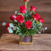 Red roses arranged in a gold square vase with eucalyptus accents