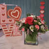 Pink and red floral arrangement in a glass vase with heart decorations