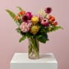 Mixed bouquet of pink, orange, and yellow flowers in a clear glass vase