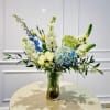 Tall floral arrangement in a clear glass vase with blue, white, and pale yellow blooms