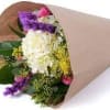 Hand-tied bouquet of white hydrangea with purple, yellow, and pink blooms wrapped in brown kraft paper.