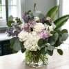 Mixed bouquet of white, blush, and purple flowers in a glass vase