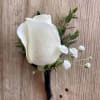 White rose boutonniere with small white filler flowers and greenery