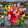 Colorful bouquet of roses, calla lilies, and lilies in a clear glass vase on stone steps