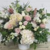 Large pastel bouquet with roses, hydrangeas, and lilies in a white container