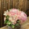 Pink floral arrangement in a square glass vase with roses and orchids