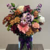Mixed bouquet of chrysanthemums and roses in a glass vase with a purple ribbon