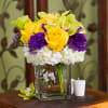 Yellow roses and purple flowers in a clear glass vase with white blooms
