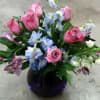Pink roses and blue flowers arranged in a dark glass vase