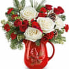 Red and white roses arranged in a red pitcher with pine accents