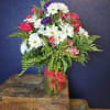 Bouquet of white daisies, pink roses, and purple blooms in a glass vase
