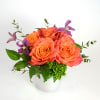 Orange roses in a white vase with purple flowers and greenery