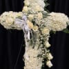 Tall white floral cross on an easel with roses and a white ribbon bow.