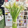 Tall bundle of white calla lilies in a clear glass vase tied with raffia