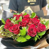 Hand-tied bouquet of red roses with small white filler flowers in black and tan wrap