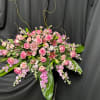 Pink roses and lilies arranged with trailing purple flowers on a black drape
