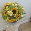 Basket arrangement of sunflowers, pale roses, and green hydrangeas with a yellow ribbon