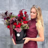 Woman holding a black box of red and burgundy flowers