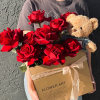 Box of red roses with a small teddy bear held in someone’s arms