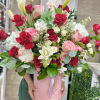 Tall arrangement of red and pink roses with white blooms and calla lilies in a pink hatbox container