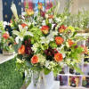 Tall hatbox arrangement with orange roses, white lilies, calla lilies, orchids, and green hydrangea