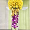 Tall glass vase with submerged purple orchids and a dome of yellow roses tied with a satin bow.