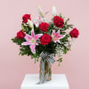 Red roses and pink lilies in a glass vase with a striped ribbon
