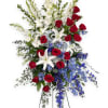 Tall standing arrangement of red roses, white lilies, and blue flowers on a metal easel