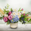 Mixed bouquet with pink roses, white orchids, and blue hydrangea in a ceramic vase