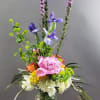 Tall mixed flower arrangement in a glass vase with pink, purple, white, and orange blooms