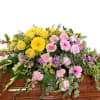 Casket spray with yellow and pink flowers and trailing greenery