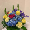 Bouquet of blue hydrangeas, yellow roses, and purple irises in a square vase