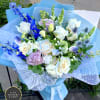 Hand-tied bouquet of white roses, blue delphinium, and pastel blooms wrapped in blue paper.