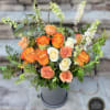 Arrangement of orange and cream roses with tall white blooms in a gray cylinder vase