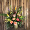 Tall tropical bouquet with orange and pink flowers in a gold vase
