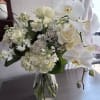 White roses, hydrangeas, and orchids arranged in a glass vase