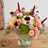 Mixed bouquet of peach roses, white anemones, and burgundy blooms in a glass vase
