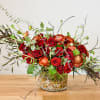 Red and orange rose arrangement in a glass vase with branches
