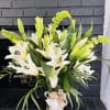 White lilies and green blooms in a glass vase with a burlap bow
