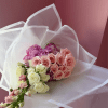 Bouquet of pink and cream roses with purple blooms wrapped in white paper