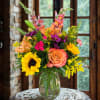 Mixed bouquet in a clear glass vase with sunflowers, roses, lilies, and snapdragons